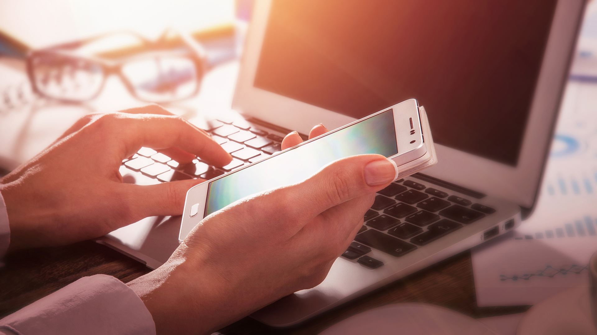 Woman holding a cell phone working on a laptop